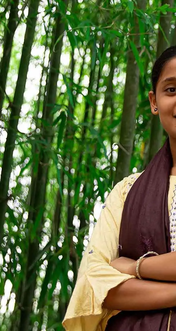 Antora, 16, standing against a background of bamboo trees in her home district of Rangpur in Bangladesh.