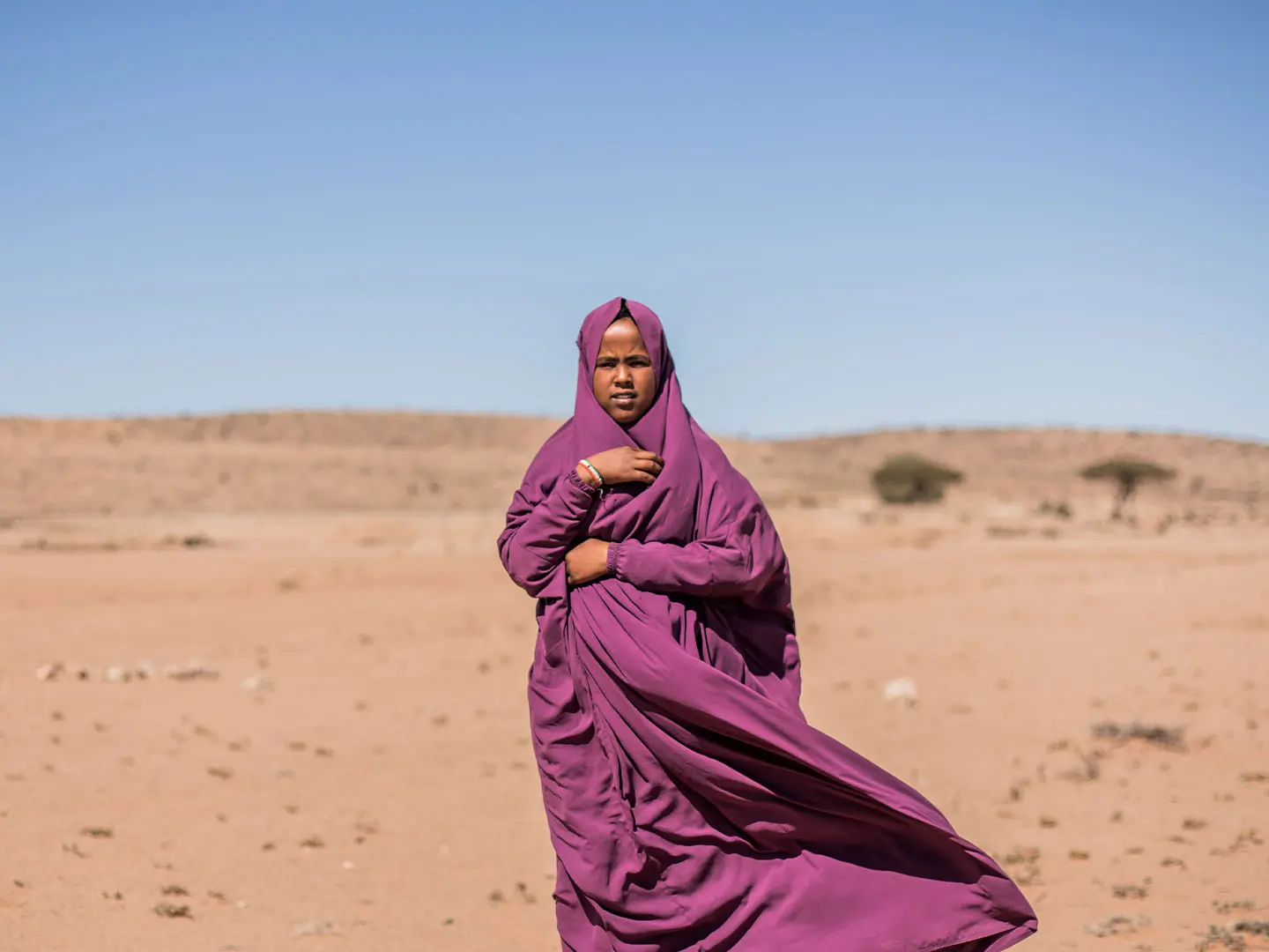 Hamda standing outside in sandy landscape wearing purple robes/headscarf