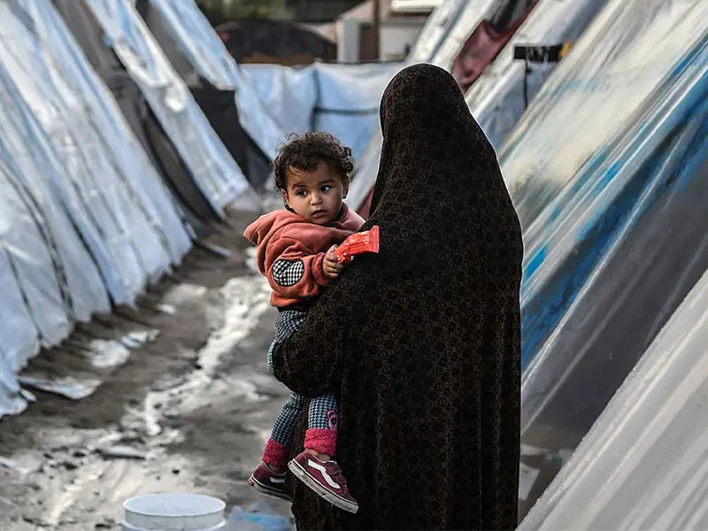 Woman holding child among tents in Gaza