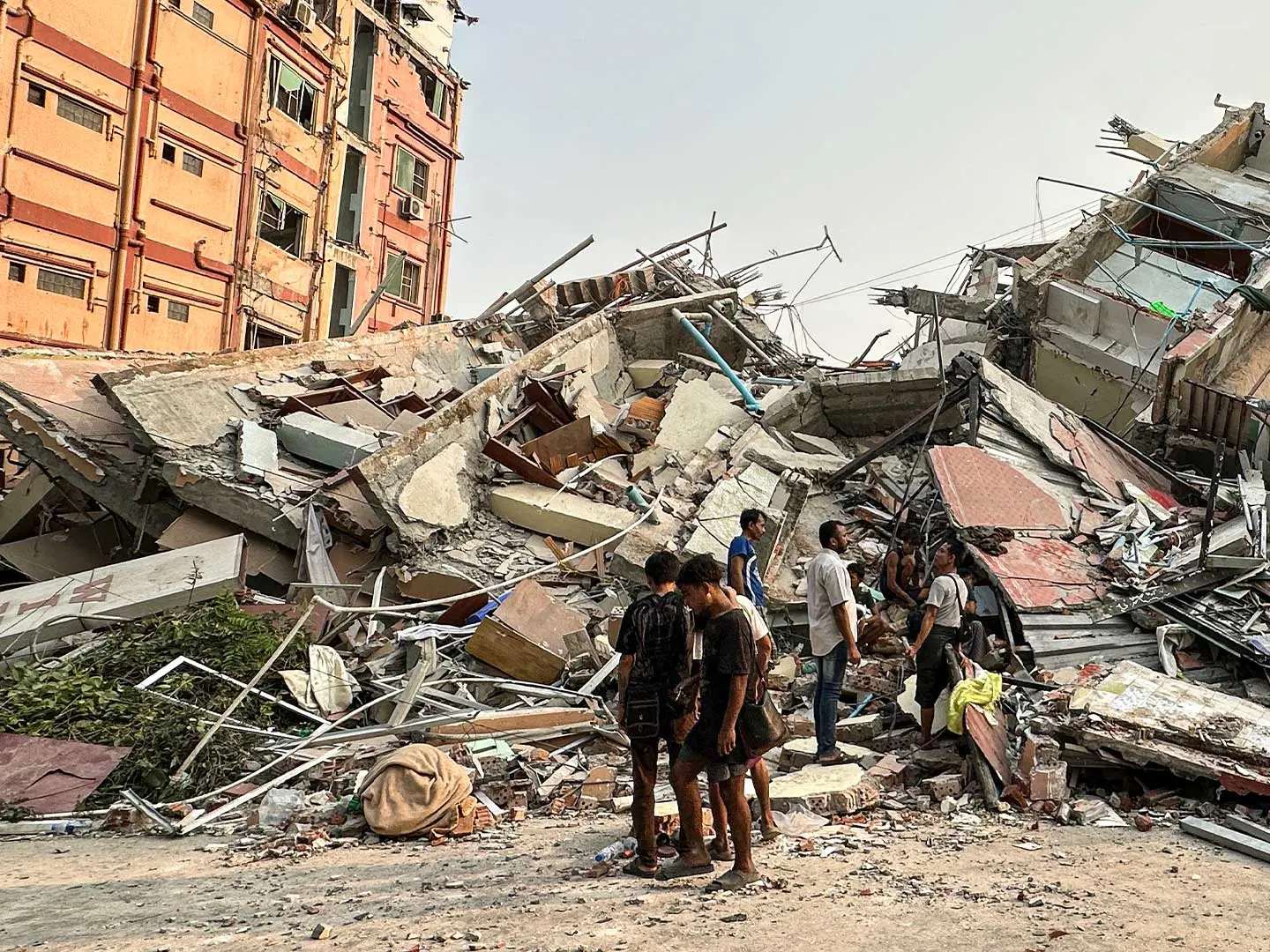 Children and adults standing among collapsed buildings and rubble following Myanmar earthquake.