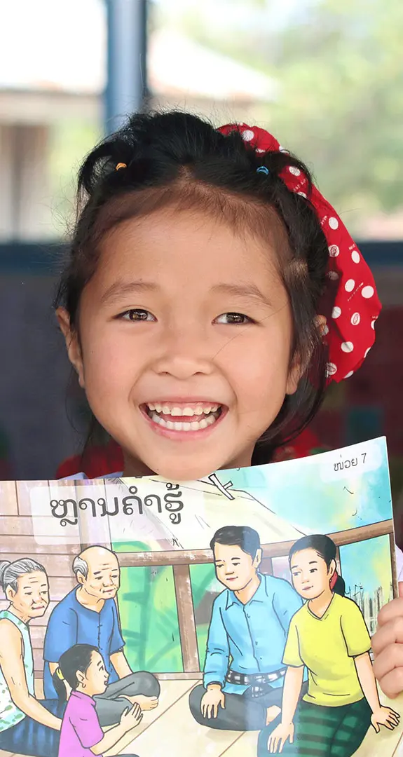 Anna smiling at camera and holding a book that is helping her learn how to read