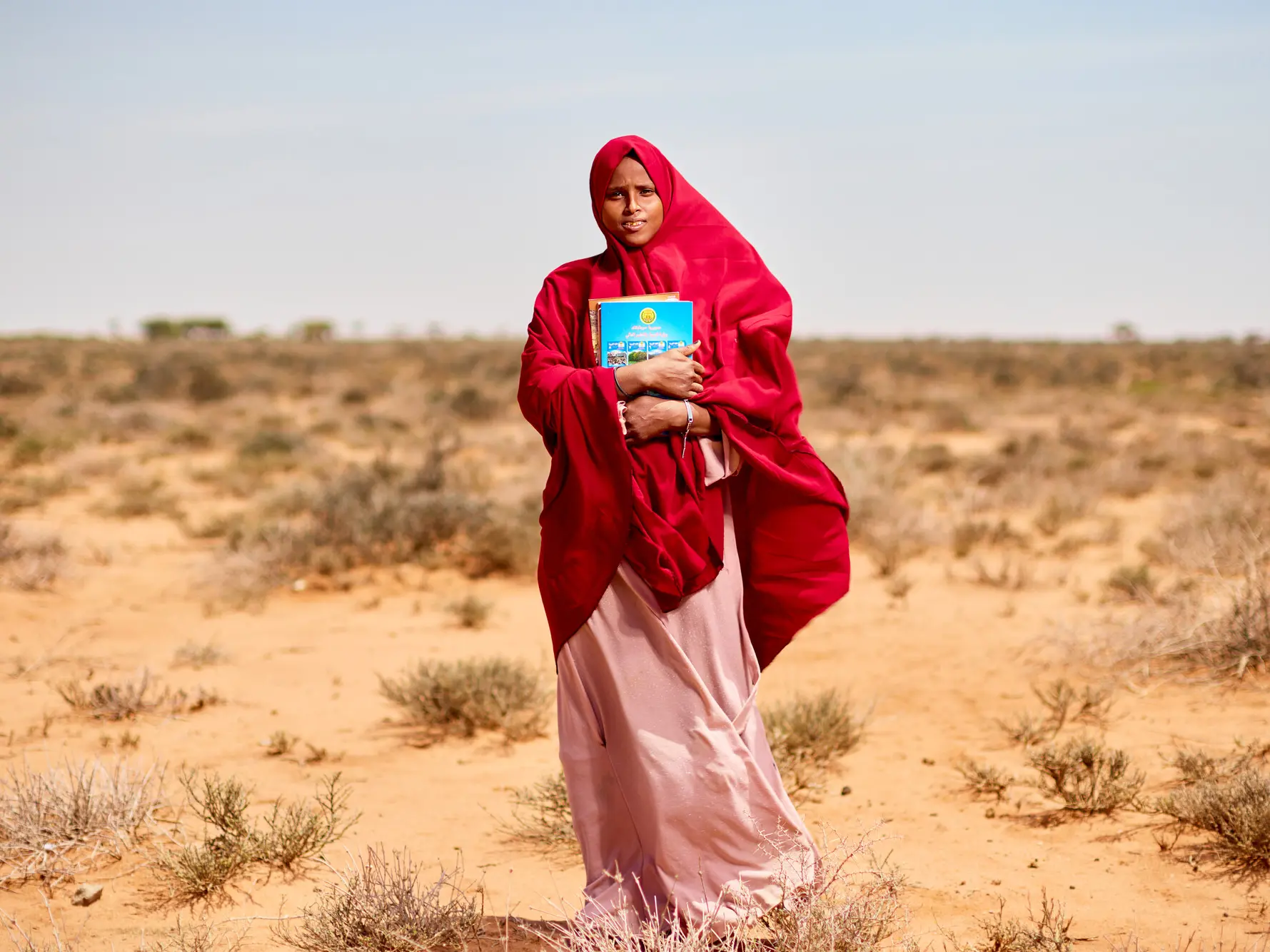 Hibbaq, 18, standing in the bush holding her school books in Somalia.