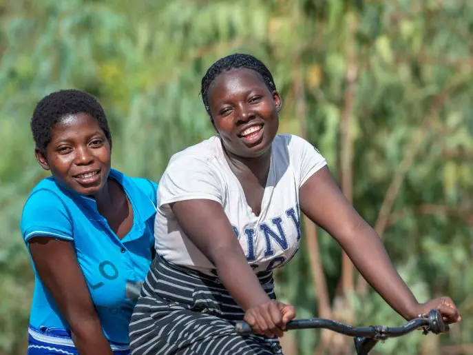 Loveness and Shakira, two young women from Malawi, riding on a bike and smiling